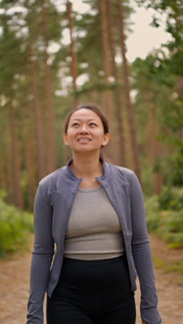 Vertical-Video-Of-Woman-Wearing-Sports-Clothing-Exercising-Looking-Around-Walking-Along-Track-In-Forest-Enjoying-Peace-And-Beauty-Of-Nature-Shot-In-Real-Time